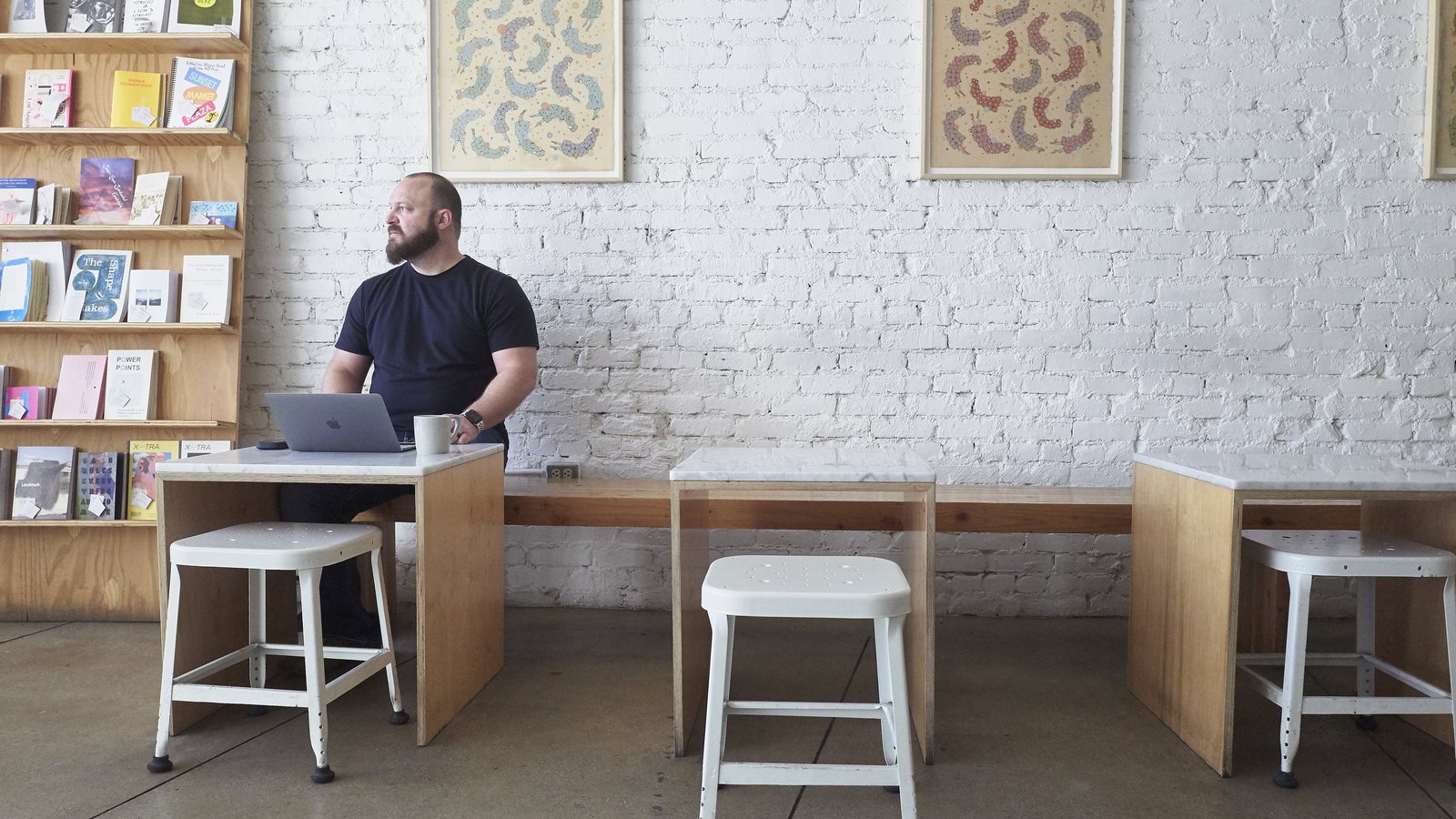 Josh Aragon working alone at a marble table in a quiet coffee shop, laptop open, looking out of frame.